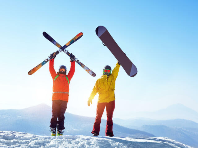 Snowboarder und Skifahrer halten Ski und Snowboard in die Luft