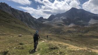 Eine MTB-Gruppe in der Abfahrt auf einem Single-Trail mit der Tessiner Bergwelt im Hintergrund.