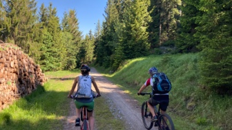 Zwei Mountainbiker*innen während der Tour im Bayerischen Wald mit dem Wald im Hintergrund.