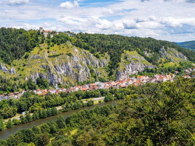 Ein Fluss schlängelt sich durch das Talbett des Altmühltals mit den Felsen im Hintergrund.