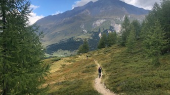 Eine Gruppe an Moutainbiker in der Tessiner Bergwelt auf einem Trail mit den imposanten Gipfeln im Hintergrund.