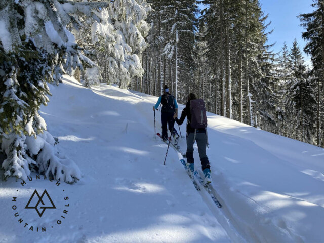 Zwei Frauen auf einer Skitour durch verschneiten Wald – Skier spuren den Weg durch frischen Pulverschnee in den Alpen.