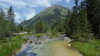 Ein Alpenfluss schlängelt sich durch das Tal mit Berge im Hintergrund