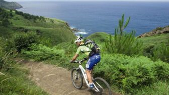 Ein Mountainbiker unterwegs in den Pyrenäen mit dem Meer im Hintergrund.