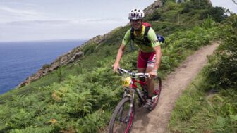 Ein Mountainbiker bei der Pyrenäen-Durchquerung auf einem Singletrail mit dem Meer im Hintergrund.